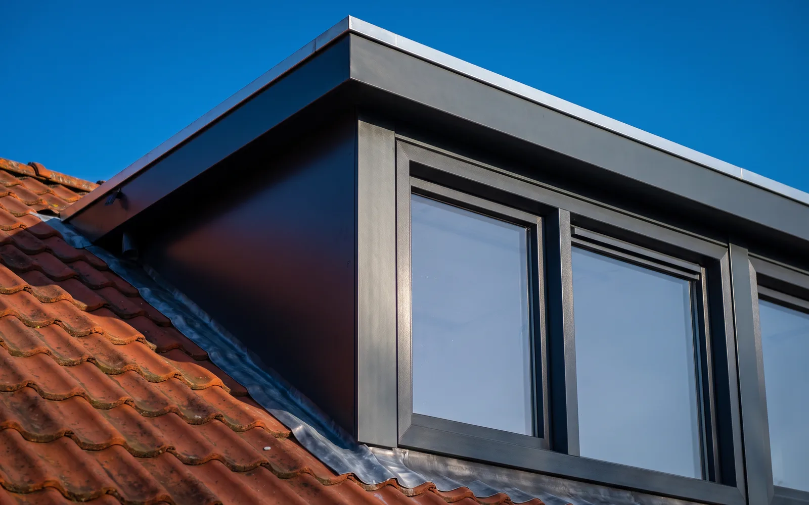 Detail van een nieuwe dakkapel met antraciet kozijnen en een strakke zinken rand