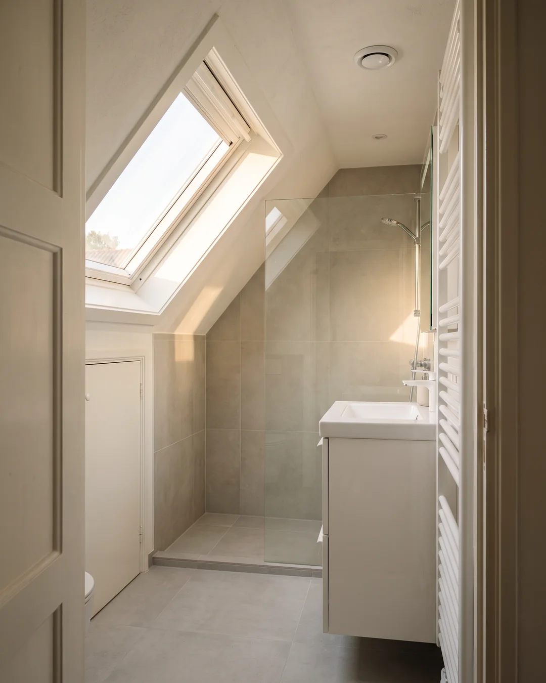 Een verbouwde zolder met een nieuwe badkamer onder het schuine dak, met een ventilatiepunt in het plafond