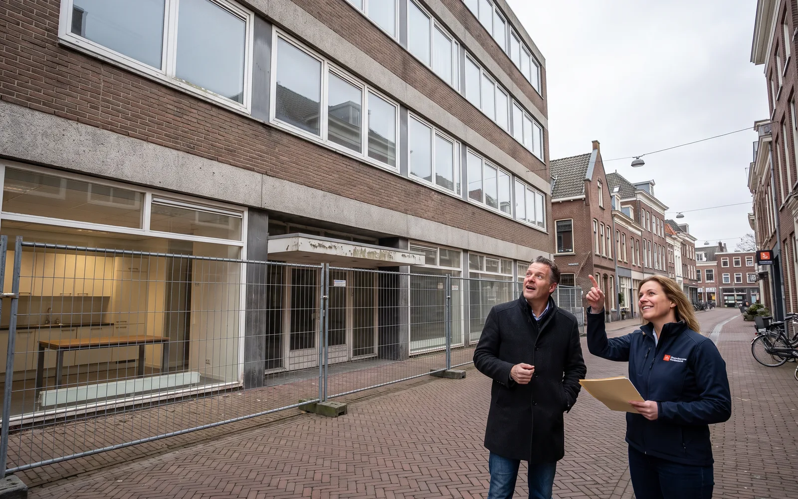 Onze kostendeskundige en een ontwikkelaar kijken vanaf de stoep naar een leeg kantoorgebouw