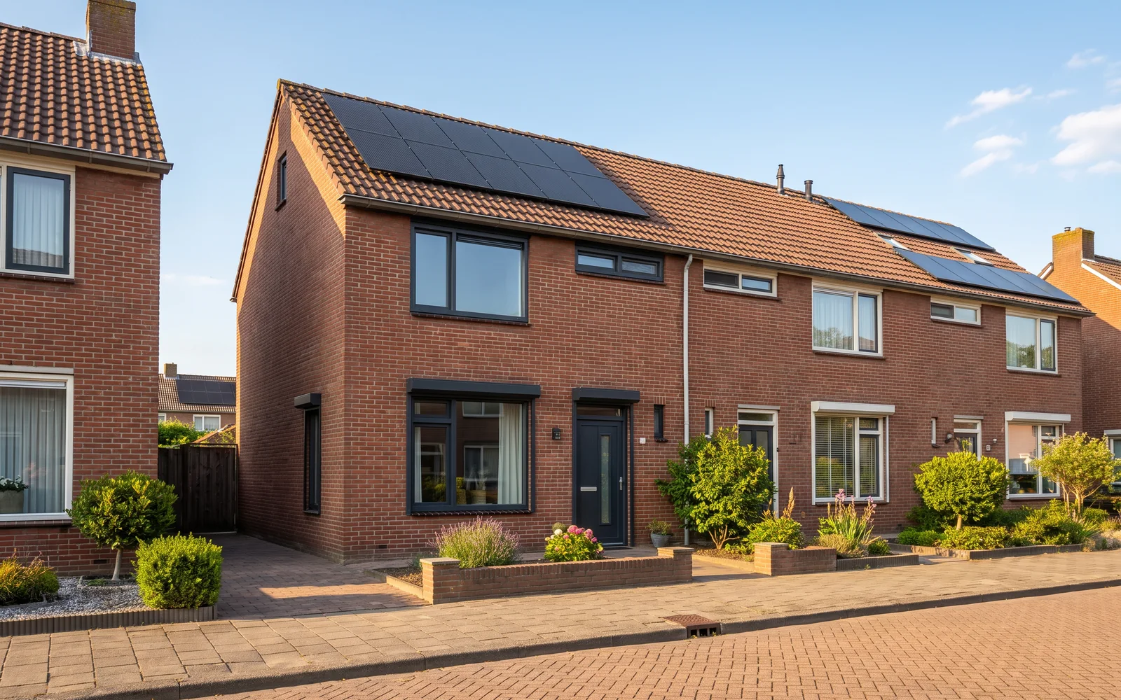 Een rijwoning uit de jaren zeventig in de middagzon, met nieuwe antraciet kozijnen en zonnepanelen op het dak